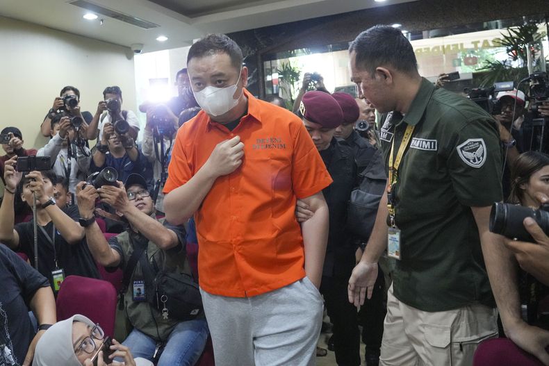 Agentes de inmigración llevan a un fugitivo chino identificado sólo por sus iniciales LQ a una conferencia de prensa en Yakarta, Indonesia, el jueves 10 de octubre de 2024. (AP Foto/Tatan Syuflana)