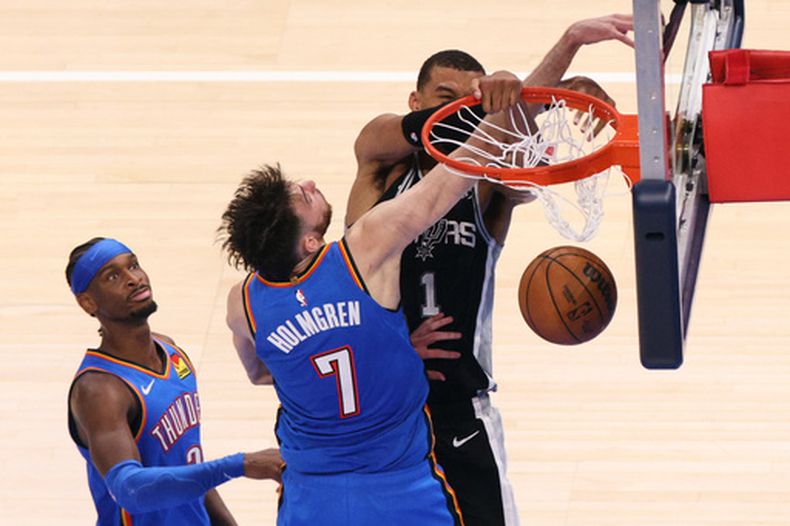 Victor Wembanyama (1), de los Spurs de San Antonio, clava el balón mientras recibe una falta por parte de Chet Holmgren (7), del Thunder de Oklahoma City, durante el segundo tiempo extra en el primer juego de las Finales de la Conferencia Oeste de los playoffs del baloncesto de la NBA, el lunes 18 de mayo de 2026, en Oklahoma City. (AP Foto/Nate Billings)