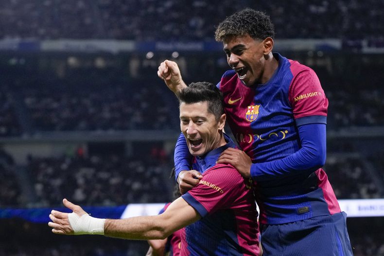 Robert Lewandowski, del Barcelona, celebra después de anotar el segundo gol de su equipo con Lamine Yamal, a la derecha, durante un partido de fútbol de La Liga española entre el Real Madrid y el Barcelona en el estadio Santiago Bernabéu en Madrid, España, el sábado 26 de octubre de 2024. (AP Foto/Manu Fernández)
