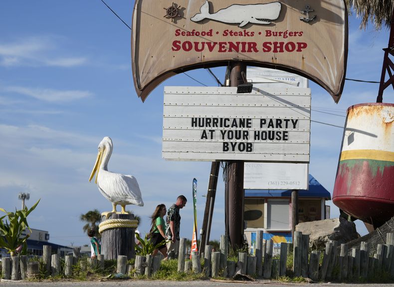 Visitantes pasan junto a un restaurante cerrado antes del paso de la tormenta Beryl, el sábado 6 de julio de 2024 en Port Aransas, Texas. El cartel dice Fiesta de huracán en tu casa, lleva tu propia bebida. (AP Foto/Eric Gay)