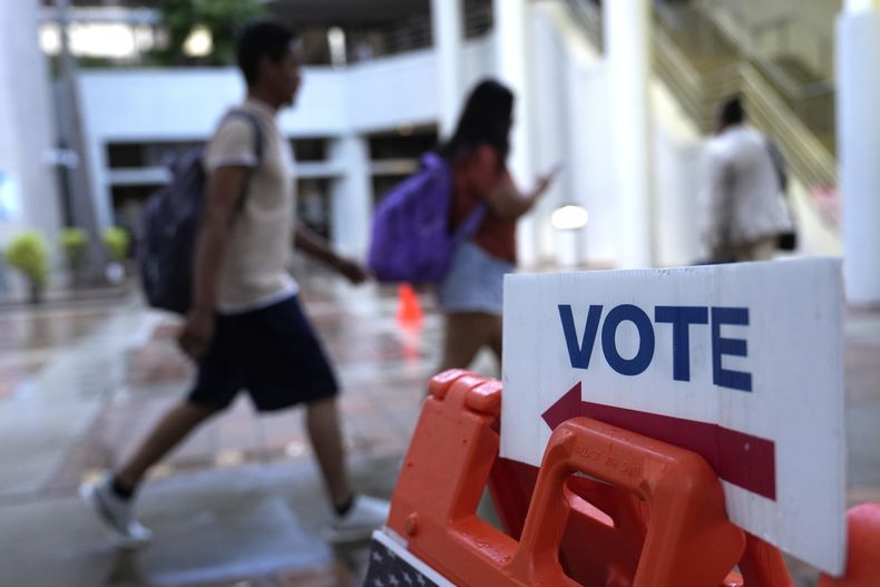 Unas personas caminan junto a un letrero para votar en el primer día de la votación anticipada de las elecciones generales de Estados Unidos, el 21 de octubre de 2024, en Miami. (AP Foto/Lynne Sladky, Archivo)