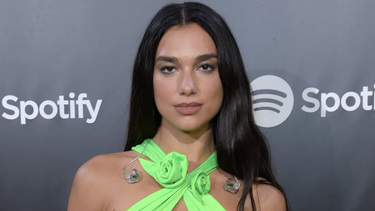 sin sosten, dua lipa luce su cuerpo usando un vestido negro lleno de cortes