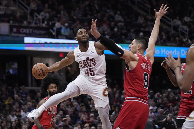Donovan Mitchell (45), de los Cavaliers de Cleveland, pasa el balón alrededor del pívot de los Bulls de Chicago, Nikola Vucevic (9), en la segunda mitad del juego de baloncesto de la NBA, el lunes 15 de enero de 2024, en Cleveland. (AP Foto/Sue Ogrocki)
