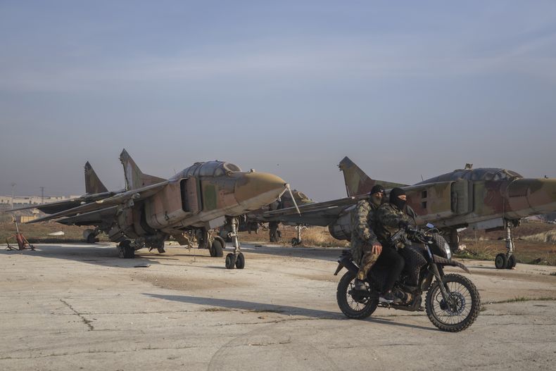 Combatientes opositores sirios a bordo de una motocicleta frente a aviones del ejército sirio en el aeropuerto militar de Al-Nayrab después de asumir el control de las instalaciones, el lunes 2 de diciembre de 2024, a las afueras de Alepo, Siria. (AP Foto/Omar Albam)