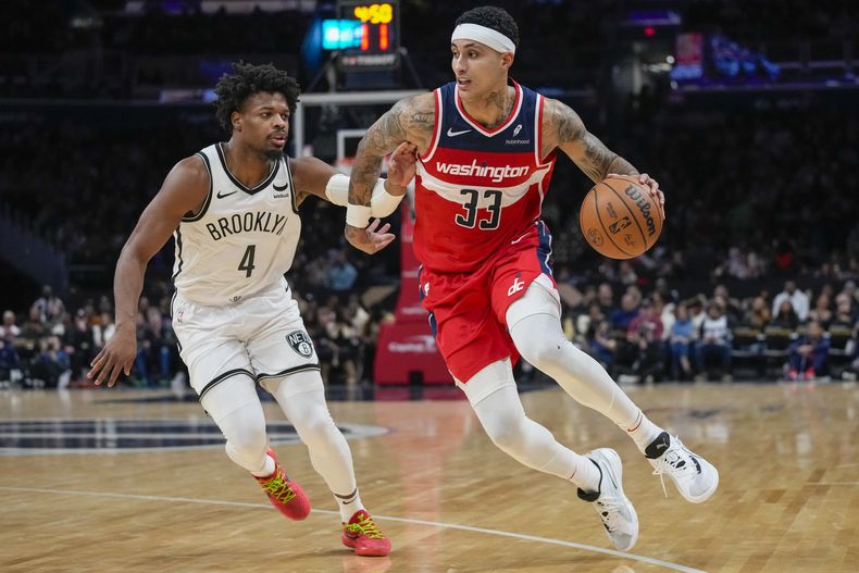 El alero de los Wizards de Washington Kyle Kuzma (33) conduce y rebasa al armador de los Nets de Brooklyn Dennis Smith Jr. (4) durante la 2da mitad del juego de la NBA el viernes 29 de diciembre de 2023, en Washington. (AP Foto/Alex Brandon)