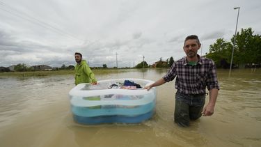 Dos hombres usan una alberca inflable para transportar sus pertenencias en un camino inundado de Lugo, Italia, el jueves 18 de mayo de 2023. (AP Foto/Luca Bruno)