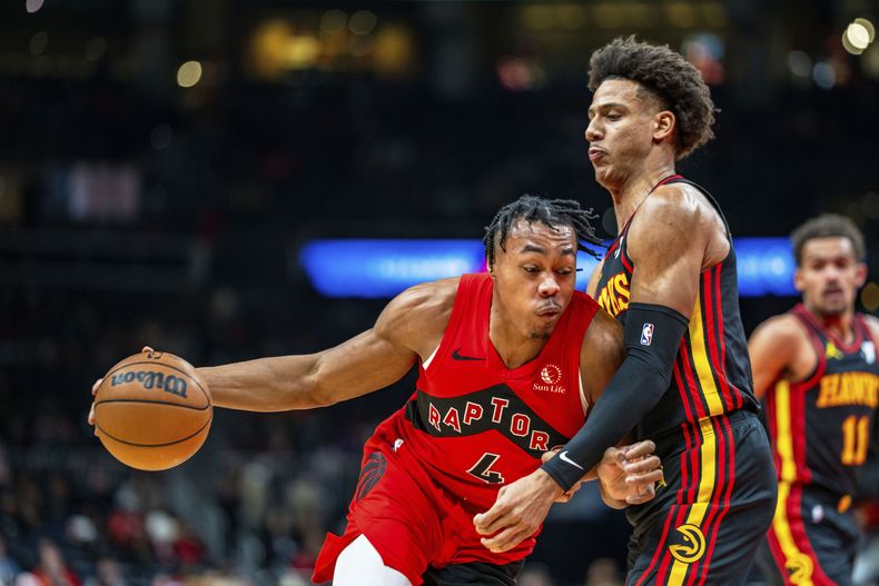 Scottie Barnes (4), de los Raptors de Toronto, lleva el balón mientras es marcado por Jalen Johnson (1), de los Hawks de Atlanta, duranta la primera mitad del juego de baloncesto de la NBA el viernes 23 de febrero de 2024, en Atlanta. (AP Foto/Jason Allen)