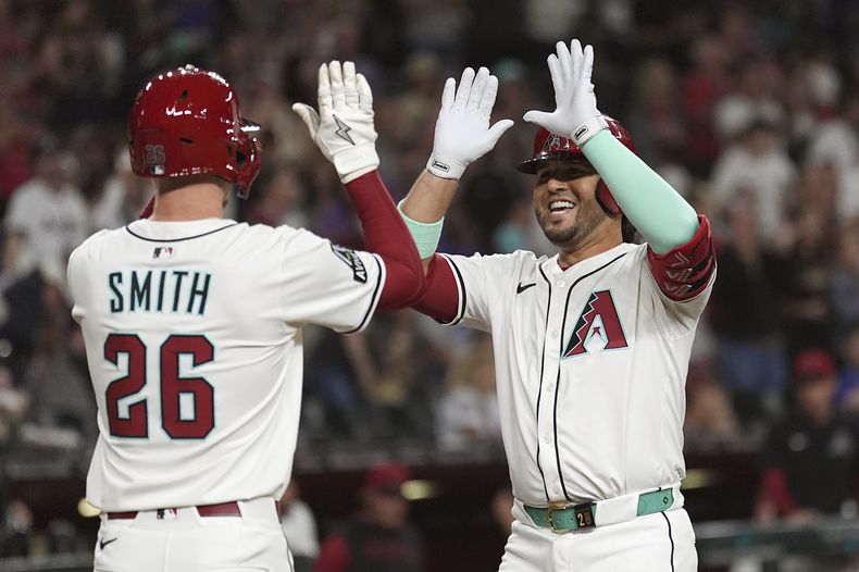 Eugenio Suárez, derecha, de los Diamondbacks de Arizona, sonríe mientras celebra un cuadrangular de dos carreras frente con Pavin Smith (26) durante la segunda entrada del juego de béisbol ante los Cachorros de Chicago, el viernes 28 de marzo de 2025, en Phoenix. (AP Foto/Ross D. Franklin)