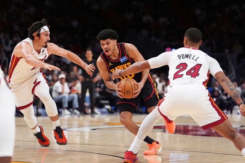 Rayj Dennis, centro, de los Hawks de Atlanta, lleva el balón bajo presión entre Jaime Jaquez Jr., izquierda, y Norman Powell (24), del Hear de Miami, durante la primera mitad del juego de baloncesto de la NBA, el domingo 12 de abril de 2026, en Miami. (AP Foto/Rebecca Blackwell)