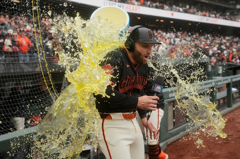 Casey Schmitt de los Gigantes de San Francisco es empapado por Willy Adames mientras es entrevistado después de un partido de béisbol contra los Marlins de Miami, el sábado 25 de abril de 2026, en San Francisco. (AP Foto/Jeff Chiu)