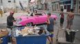 Un hombre recoge basura mientras los turistas viajan en un automóvil clásico estadounidense durante un apagón en La Habana, Cuba, el miércoles 3 de diciembre de 2025. (AP Foto/Ramón Espinosa)