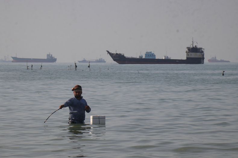 Un hombre de pie en el mar, aparentemente pescando, mientras buques graneleros, de carga y barcos de servicio se alinean en el horizonte del estrecho de Ormuz, frente a la costa de Bandar Abbas, Irán, el lunes 27 de abril de 2026.(Razieh Poudat/ISNA vía AP)