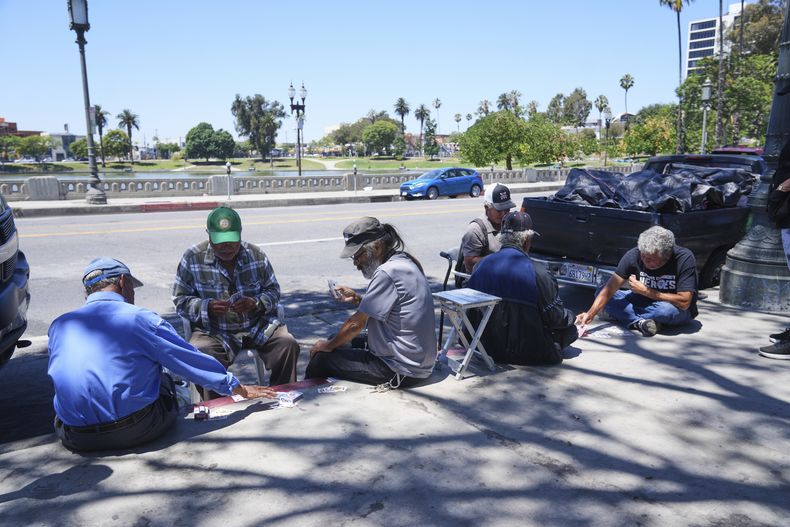 Varias personas juegan cartas en una acera del Parque MacArthur, el martes 8 de julio de 2025, en Los Ángeles. (AP Foto/Damian Dovarganes)