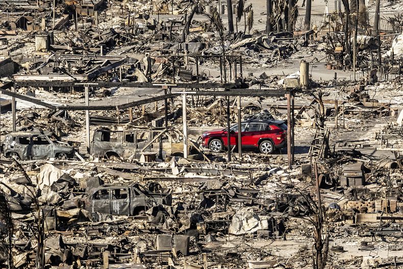 Un automóvil pasa junto a casas y vehículos destruidos por el incendio de Pacific Palisades Bowl Mobile Estates, el domingo 12 de enero de 2025, en Los Ángeles. (AP Foto/Noah Berger)
