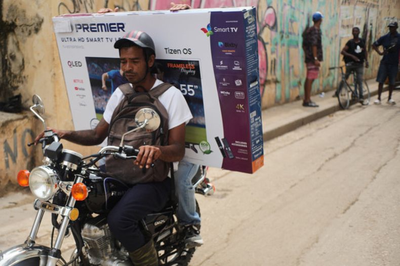 Un motociclista transporta a un cliente con un televisor en una caja durante un apagón en La Habana, el martes 17 de marzo de 2026. (AP Foto/Ramón Espinosa)