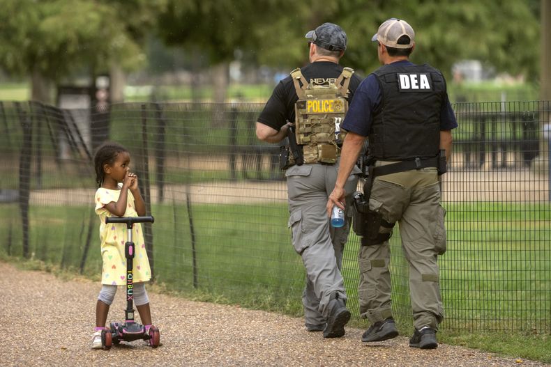 Una niña observa a los agentes de la Administración de Control de Drogas de Estados Unidos mientras patrullan el complejo de monumentos National Mall, el miércoles 13 de agosto de 2025, en Washington. (AP Foto/Mark Schiefelbein)