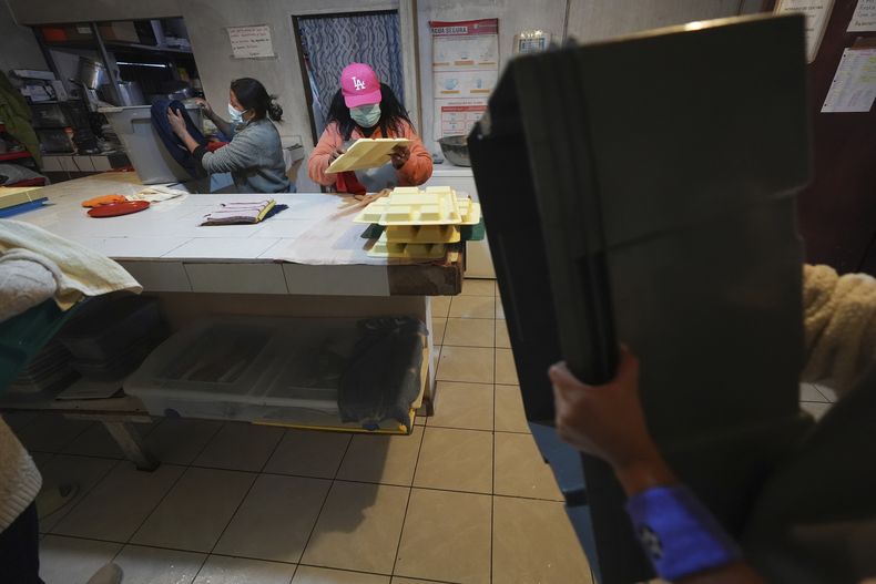 Margelis Rodríguez, de Venezuela, en el centro, limpia después de la cena en el refugio de migrantes donde vive con sus dos hijos en Tijuana, México, el vienes 31 de enero de 2025. (AP Foto/Gregory Bull)