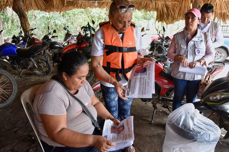 La cubana Julia Margarita Bravo Díaz, con chaleco salvavidas, muestra fotos de personas desaparecidas, incluyendo a su hija Meiling Álvarez Bravo y su nieto Samei Armando Reyes Álvarez, a los residentes locales en San José Hueyate, estado de Chiapas, México, el sábado 9 de mayo de 2026 durante una búsqueda de migrantes que desaparecieron a finales de 2024 a lo largo de una ruta marítima de contrabando hacia Estados Unidos. (AP Foto/Edgar H. Clemente)