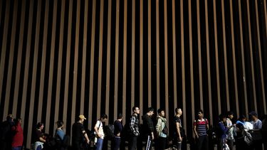 ARCHIVO - Personas formadas junto a un muro fronterizo mientras esperan solicitar asilo en Estados Unidos tras cruzar la frontera desde México, el martes 11 de julio de 2023, cerca de Yuma, Arizona. (AP Foto/Gregory Bull, Archivo)
