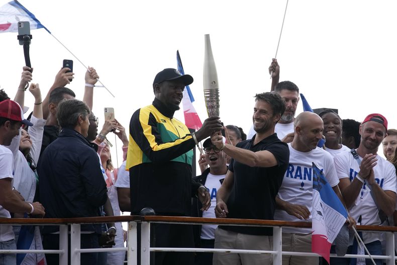 Tony Estanguet (derecha), el presidente del comité organizador de los Juegos Olímpicos de París 2024, entrega a la antorcha a Usain Bolt, el martes 25 de julio de 2023, en París. (AP Foto/Christophe Ena)