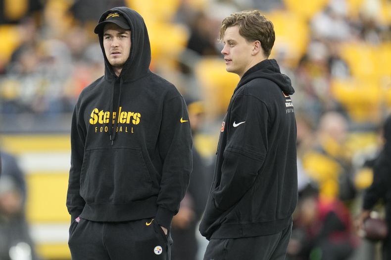El quarterback de ls Steelers de Pittsburgh Kenny Pickett y el quarterback de los Bengals de Cincinnati Joe Burrow observan el calentamiento antes del encuentro del sábado 23 de diciembre del 2023. (AP Foto/Gene J. Puskar)