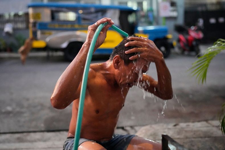 El conductor de Jeepney Edgar Funelas se lava en una calle junto al jeepney donde viven él y su hija de 10 años en Quezon City, Filipinas, el viernes 10 de abril de 2026. (AP Foto/Aaron Favila)