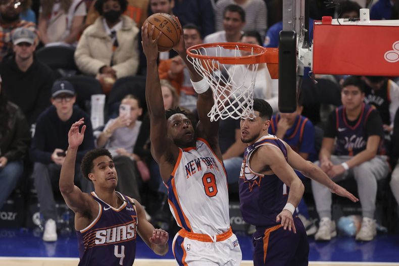 OG Anunoby (8), de los Knicks de Nueva York, clava el balón frente a Oso Ighodaro (4) y Devin Booker, derecha, durante la segunda mitad del juego de balonesto de la NBA, el domingo 6 de abril de 2025, en Nueva York. (AP Foto/Pamela Smith)