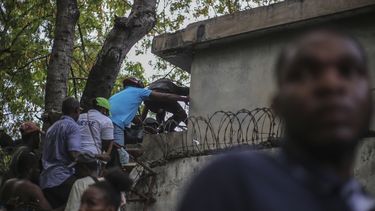 Periodistas se encaraman sobre una pared para evitar disparos de una pandilla en el Hospital General en Puerto Príncipe, el 24 de diciembre del 2024. (AP foto/Jean Feguens Regala)