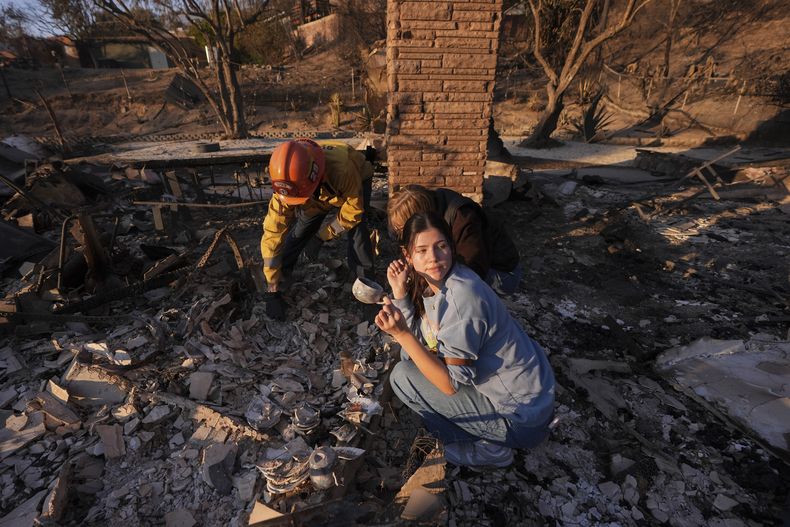 Ella Venne, al frente, sostiene una taza que encontró entre los restos de la casa de su familia , destruida por el incendio Eaton, en Glendale, mientras busca con el capitán de bomberos Chris Jernegan, a la izquierda, y su esposa, Alison, en Altadena, California, el sábado 11 de enero de 2025. (AP Photo/Mark J. Terrill)