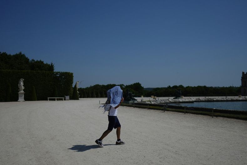 Un hombre se protege del sol mientras camina por el jardín del Palacio de Versalles, a las afueras de París, durante una ola de calor con temperaturas que superan los 40 grados Celsius (104 Fahrenheit), el lunes 22 de junio de 2026. (Foto AP/Thibault Camus)