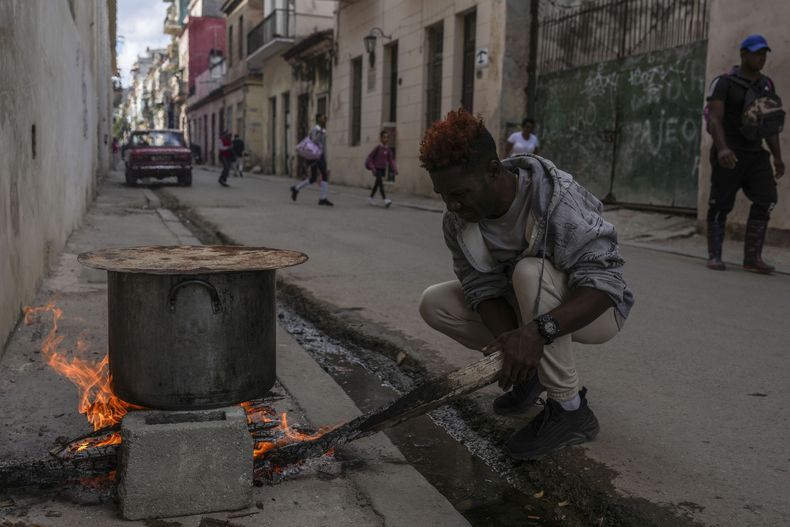 Un hombre cocina sopa sobre una fogata en una acera durante un apagón en La Habana, Cuba, el miércoles 4 de diciembre de 2024. (AP Foto/Ramón Espinosa)