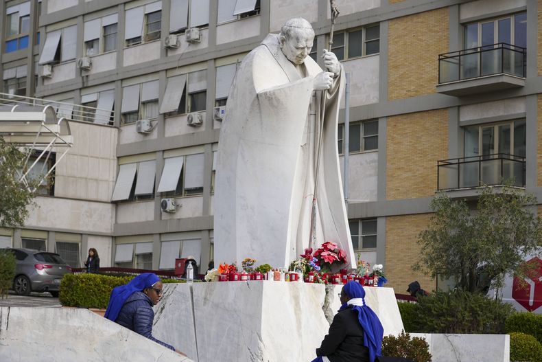 Dos monjas, sentadas junto a una estatua de san Juan Pablo II, frente al hospital policlínico Agostino Gemelli, en Roma, el 17 de febrero de 2025, donde el papa Francisco está hospitalizado debido a una bronquitis. (AP Foto/Andrew Medichini)