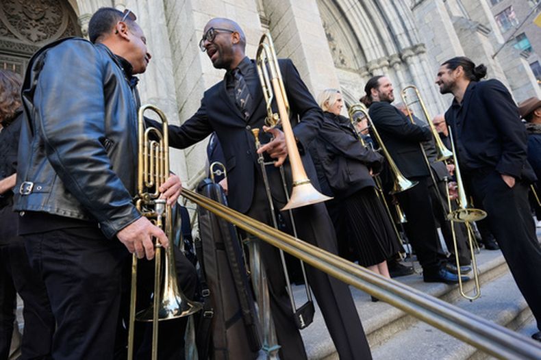 Un grupo de músicos, principalmente trombonistas, socializan y posan para calentar antes de tocar en el funeral de Willie Colón en la Catedral de San Patricio en Nueva York, el lunes 9 de marzo de 2026. (Foto AP/Seth Wenig)
