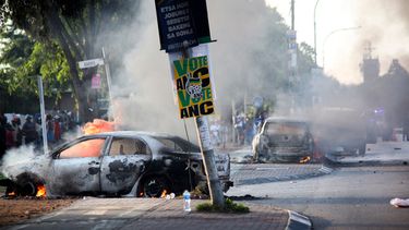 Un automóvil arde cerca de un cartel de un partido político tras haber sido incendiado durante protestas relacionadas con cuestiones migratorias en Soweto, Johannesburgo, el jueves 8 de octubre de 2026. (Foto AP)