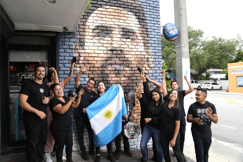 El personal del restaurante Fiorito posa frente a un mural de Lionel Messi para celebrar el anuncio de que el astro argentino jugará en la MLS, el miércoles 7 de junio de 2023, en Miami (AP Foto/Lynne Sladky)