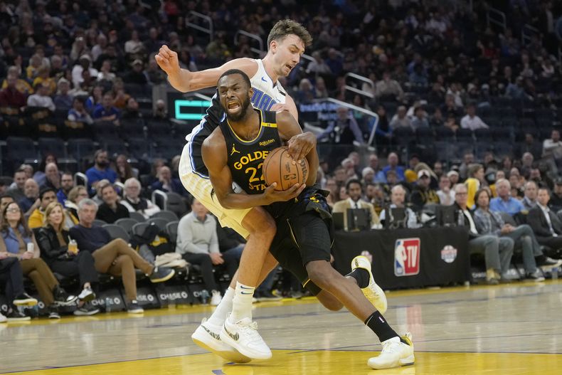 Andrew Wiggins (22) de los Warriors de Golden State, recibe una falta por parte de Franz Wagner, del Magic de Orlando, durante la segunda mitad del juego de baloncesto de la NBA, el lunes 3 de febrero de 2025, en San Francisco. (AP Foto/Jeff Chiu)