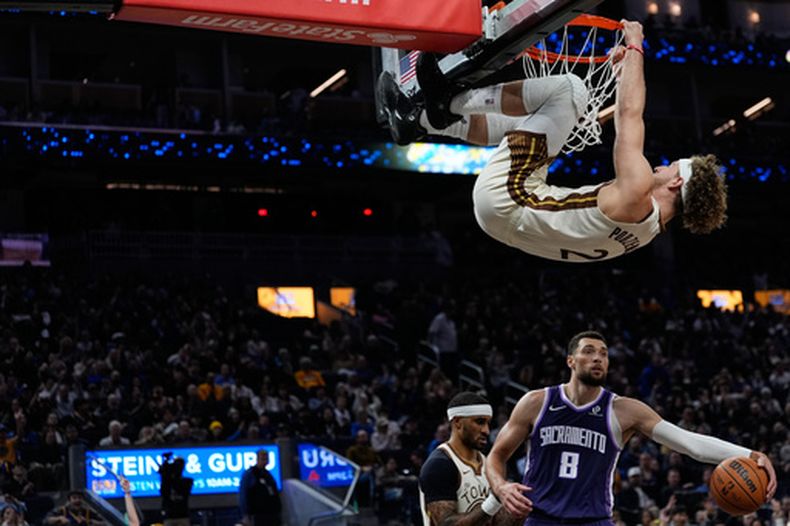 Brandin Podziemski, de los Warriors de Golden State, cuelga del aro tras una volcada ante los Kings de Sacramento, el viernes 9 de enero de 2026 (AP Foto/Godofredo A. Vásquez)