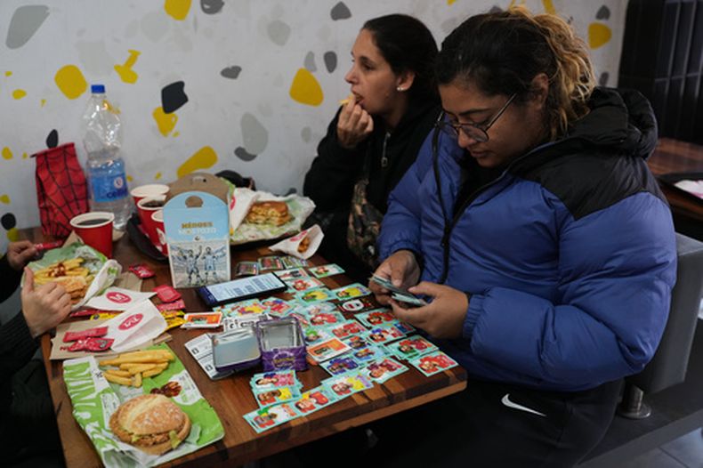 Una mujer sentada en un restaurante de comida rápida con sus cromos coleccionables de la Copa Mundial 2026 en Buenos Aires el domingo 10 de mayo del 2026. (AP Foto/Rodrigo Abd)