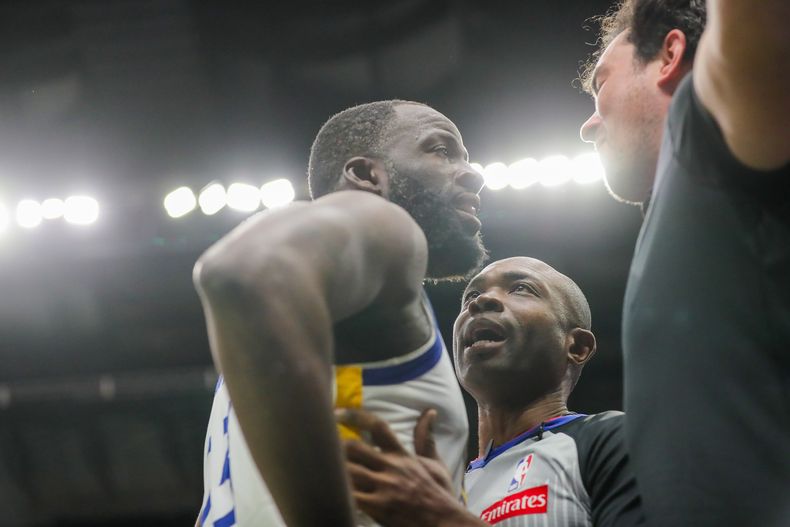 El alero de los Warriors de Golden State Draymond Green es sostenido por el árbitro Courtney Kirkland durante una confrontación con un aficionado de los Pelicans de Nueva Orleans en el encuentro del domingo 16 de noviembre del 2025. (David Grunfeld/The Times-Picayune via AP)