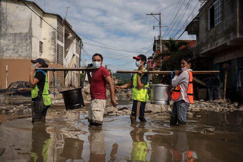 Vecinos llevan ollas con tamales donados por voluntarios para los damnificados por las recientes lluvias torrenciales por una calle inundada de Poza Rica, estado de Veracruz, México, miércoles 15 de octubre, 2025. (AP Foto/Félix Márquez)