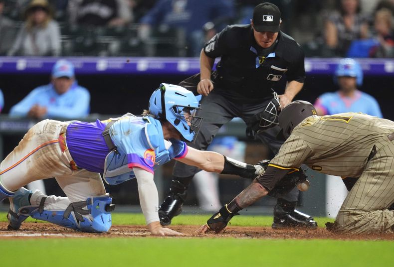 El receptor Hunter Goodman, izquierda, de los Rockies de Colorado, deja caer la pelota en el plato permitiendo que Manny Machado, derecha, de los Padres de San Diego, anote durante la sexta entrada del juego de béisbol de Grandes Ligas, el vierrnes 9 de mayo de 2025, en Denver. (AP Foto/Jack Dempsey)