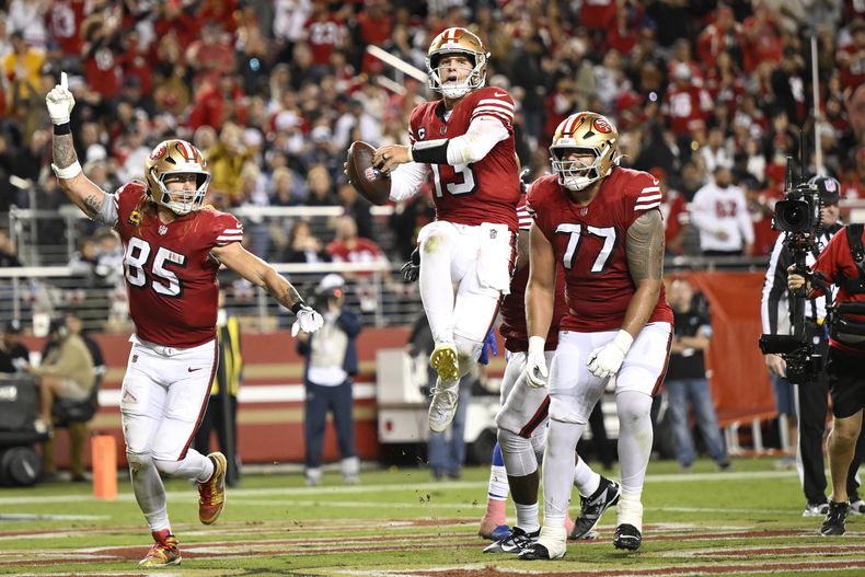 Brock Purdy, al centro, quarterback de los 49ers de San Francisco, celebra después de anotar un touchdown ante la mirada de George Kittle (85) y Dominick Puni (77), durante la segunda mitad del partido de la NFL en contra de los Cowboys de Dallas, el domingo 27 de octubre de 2024, en Santa Clara, California. (AP Foto/Eakin Howard)