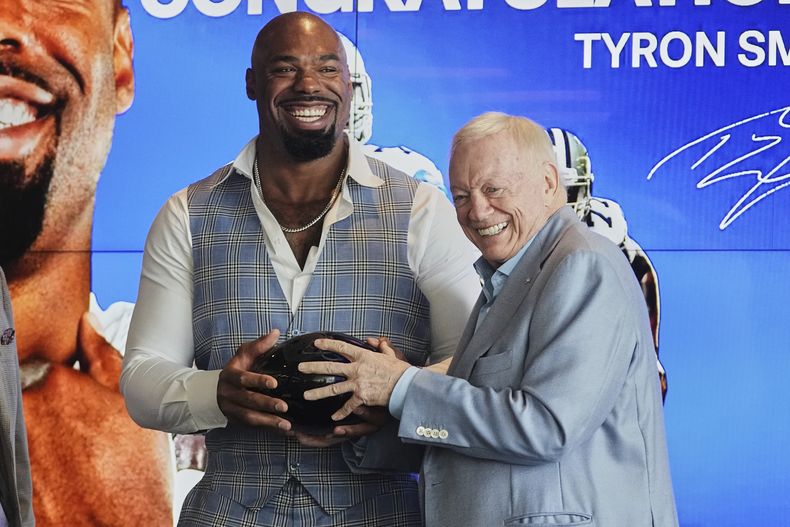 Tyron Smith, izquierda, sonríe al lado del propietario de los Cowboys de Dallasa, Jerry jones, derecha, mientras ambos sostienen un regalo que le fue entregado a Smith por parte del equipo después de una conferencia de prensa en la que Smith anunció su retiro de la NFL en las instalaciones de los Cowboys en Frisco, Texas, el miércoles 16 de abril de 2025. (AP Foto/Tony Gutierrez)