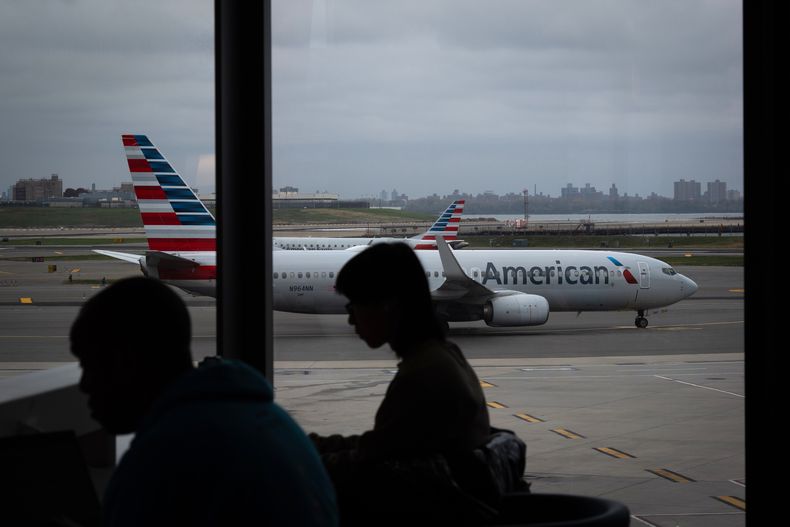 Gente esperando a vuelos mientras un avión de American Airlines circula por la pista en el aeropuerto LaGuardia (LGA) en el barrio de Queens, Nueva York, el domingo 9 de noviembre de 2025. (AP Foto/Adam Gray)