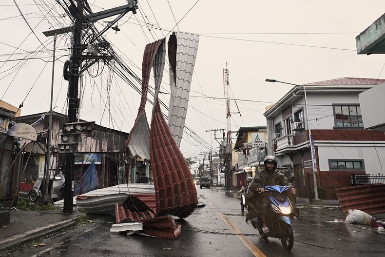 Un motorista pasa junto a un trozo de tejado colgado de cables eléctricos debido al tifón Man-yi, en una calle en el municipio de Baler, provincia de Aurora, en el nordeste de Filipinas, el lunes 18 de noviembre de 2024. (AP Foto/Noel Celis)