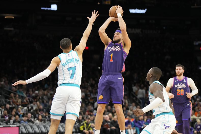 El escolta de los Suns de Phoenix Devin Booker (1) lanza sobre el escolta de los Hornets de Charlotte Bryce McGowens (7) durante la 2da mitad del juego de baloncesto de la NBA, el viernes 29 de diciembre de 2023, en Phoenix. (AP Foto/Rick Scuteri)
