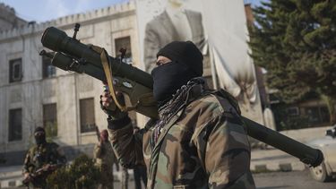 Un combatiente sirio de oposición sostiene un lanzacohetes frente a la oficina del gobierno regional, en cuya fachada se muestra una imagen del presidente sirio, Bashar Assad, rodeada de disparos, tras la toma de la ciudad de Hama por parte de la oposición, en Siria, el viernes 6 de diciembre de 2024. (AP Foto/Ghaith Alsayed)