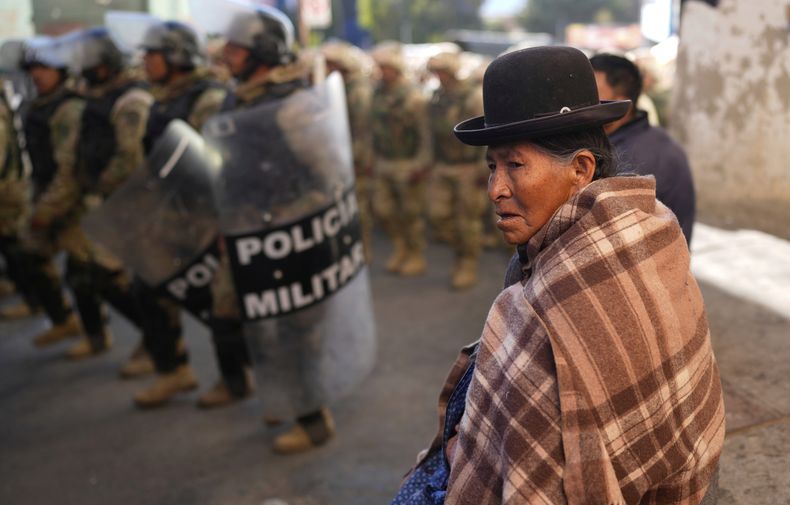 Una mujer observa a la policía militar patrullando después de que la policía pasara días despejando los bloqueos establecidos por partidarios del expresidente boliviano Evo Morales que quieren que pueda postularse nuevamente a la presidencia en Llallagua, Bolivia, el viernes 13 de junio de 2025. (AP Foto/Juan Karita)