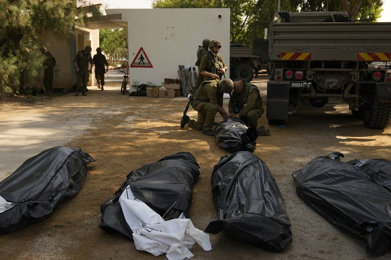 Soldados israelíes junto a los cuerpos de israelíes asesinados por combatientes de Hamas, el martes 10 de octubre de 2023, en el kibutz Kfar Aza. Combatientes de Hamas incursionaron el sábado en Kfar Aza, en donde muchos israelíes fueron asesinados o secuestrados. (AP Foto/Ohad Zwigenberg)