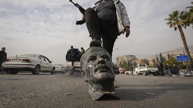 Un rebelde sirio sobre un busto de fallecido presidente sirio Hafez Assad en Damasco el 8 de diciembre del 2024. (AP foto/Hussein Malla)